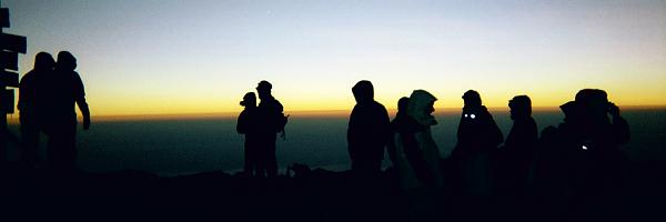Silhouettes of the group at the summit sign (left of picture), with headlights still on at sunrise